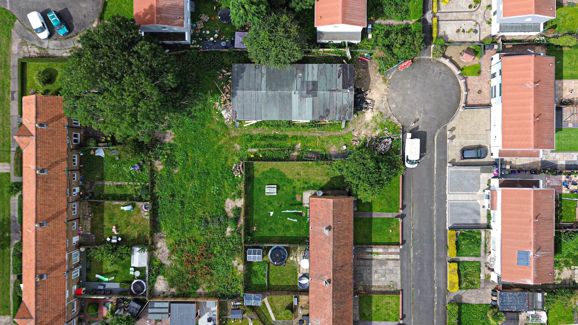 Ariel view of the Long Benton Site. Large L-shaped plot of land, at the end of a cul-de-sac covered in greenery and trees. On the land is an old, derelict, concreate prefab building that served over the years as a scout hut.