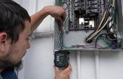 Technician using a multimeter to inspect an open electrical breaker panel and wiring