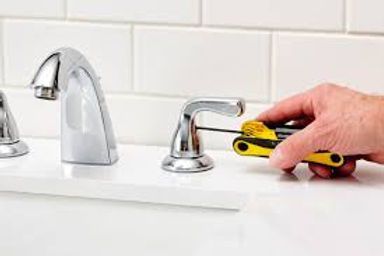 Hand tightening a sink faucet with a yellow wrench in a white bathroom sink area