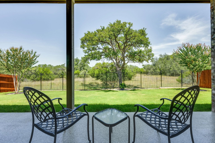 Patio chairs facing a grassy yard with trees and a fence beyond screened windows