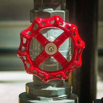 Red valve wheel on a metal pipe assembly with a clear section in the center
