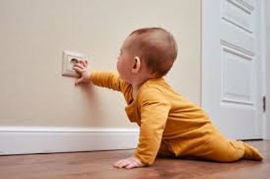 Baby crawling toward a wall outlet, reaching with one hand in a home hallway.