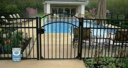 Backyard pool behind black metal fence, with blue water and a small pool sign in front.