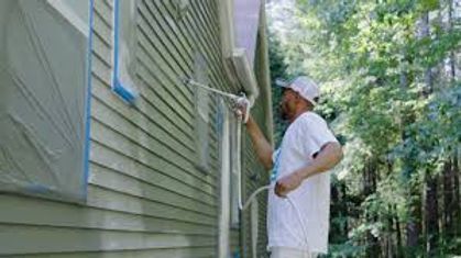 Person painting the exterior of a house with a roller on a sunny day