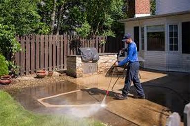 Person pressure-washing a driveway beside a house and fence on a sunny day