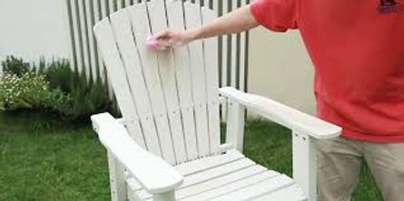 Person holding a white Adirondack chair in a grassy outdoor setting