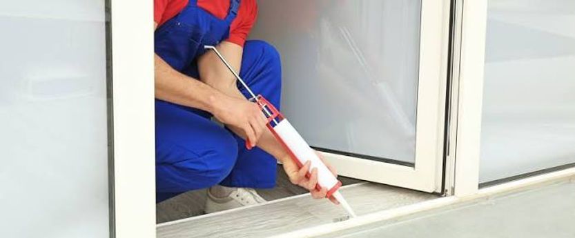 Person applying sealant with a caulking gun along the base of a white door frame