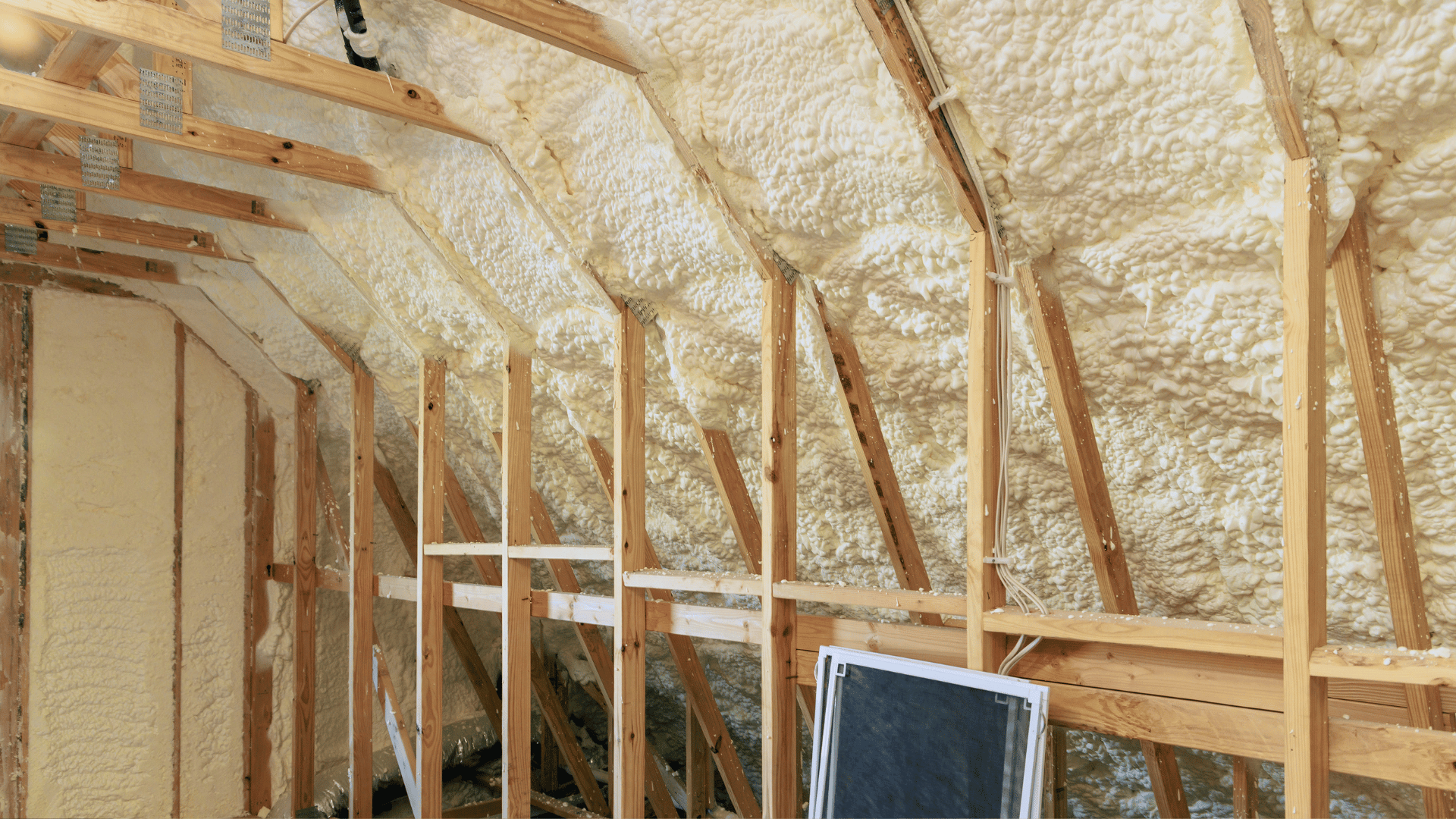 Insulated attic framing with exposed wooden studs and spray foam along the roof and walls