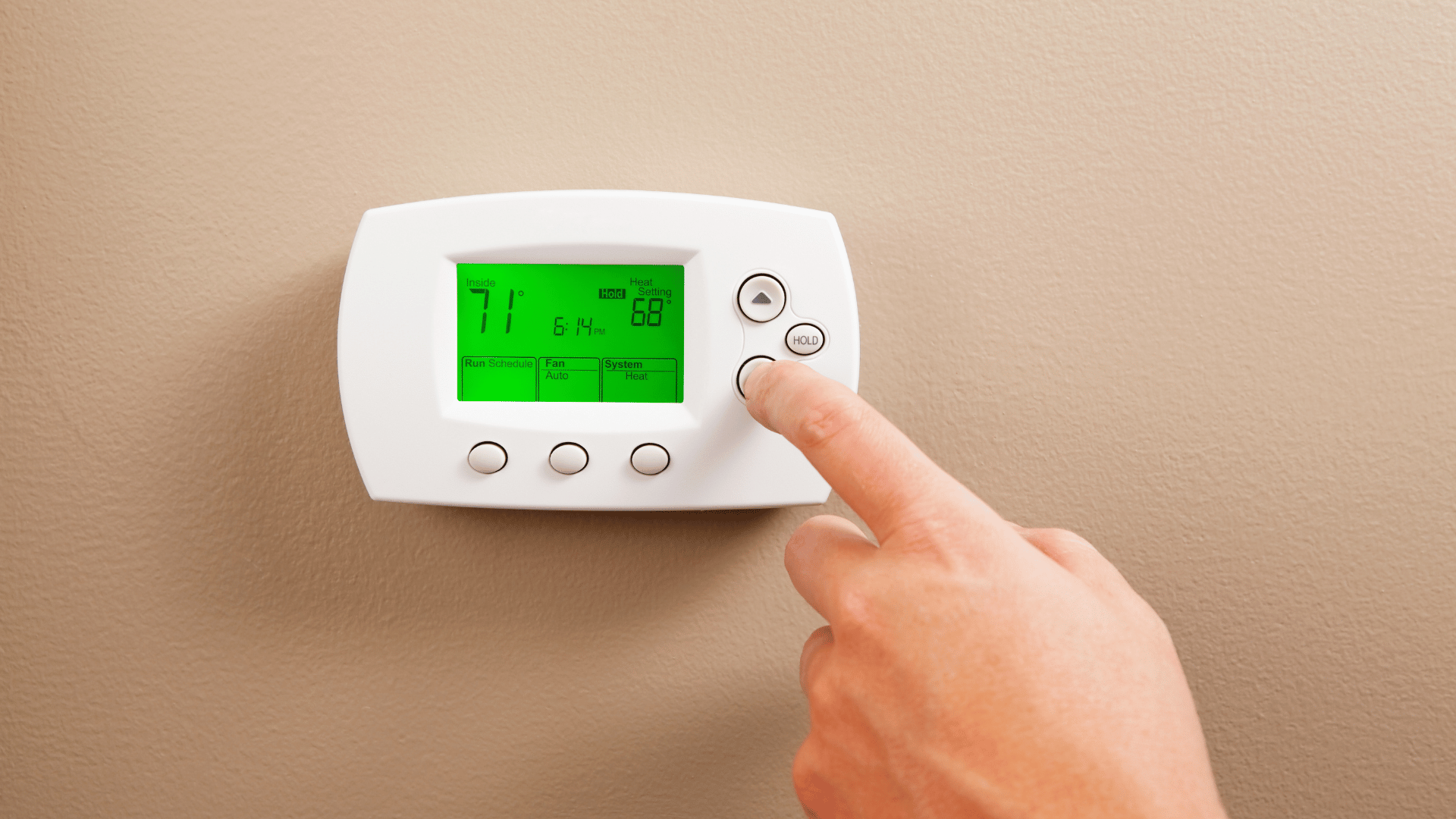 Hand pressing buttons on a white wall thermostat with a green digital display
