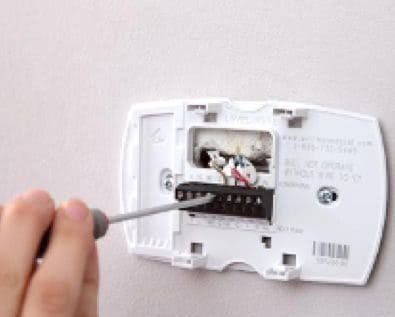 Hand unscrewing a white wall thermostat cover with a screwdriver