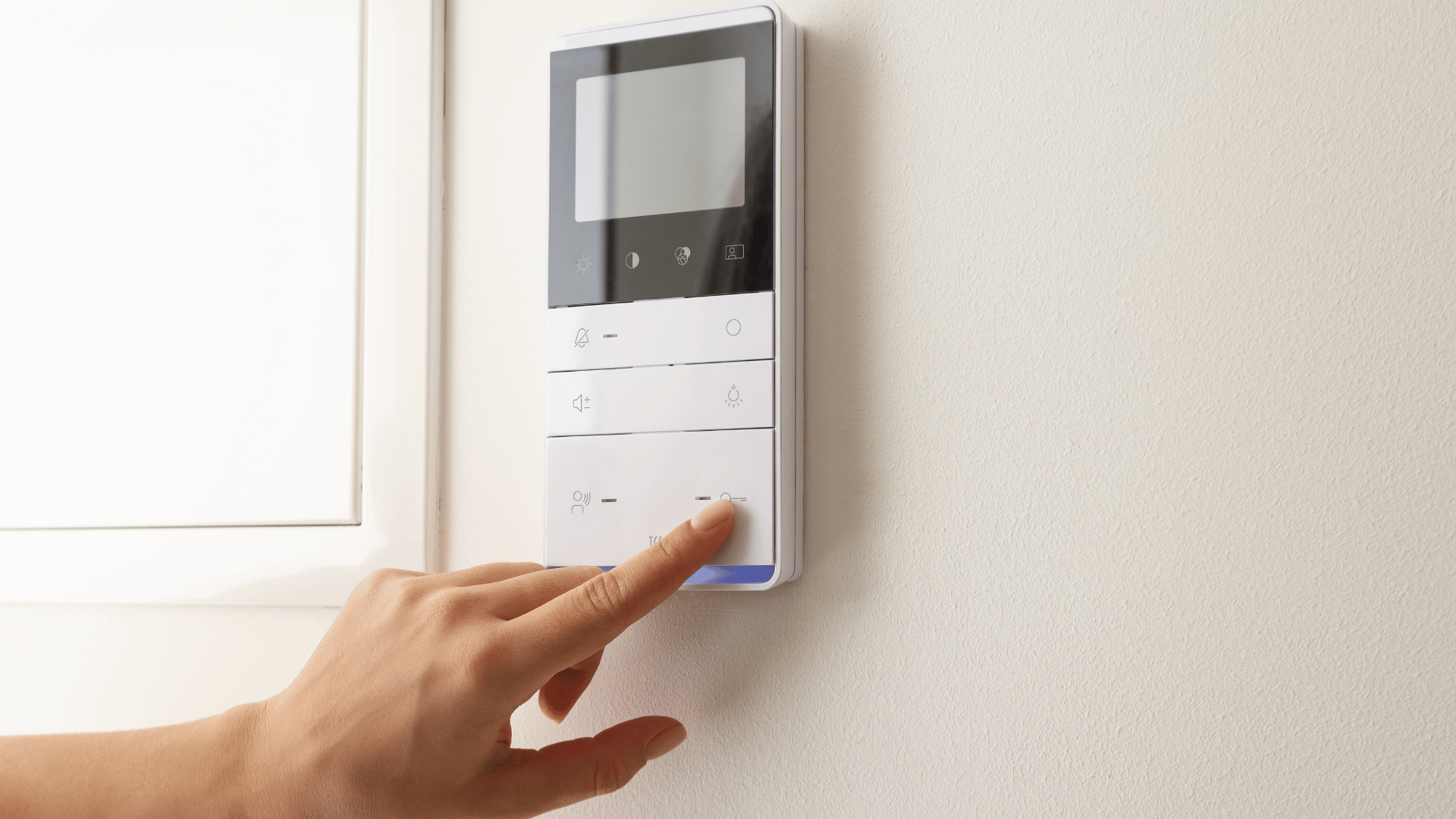 Hand pressing a blue button on a wall-mounted video intercom panel