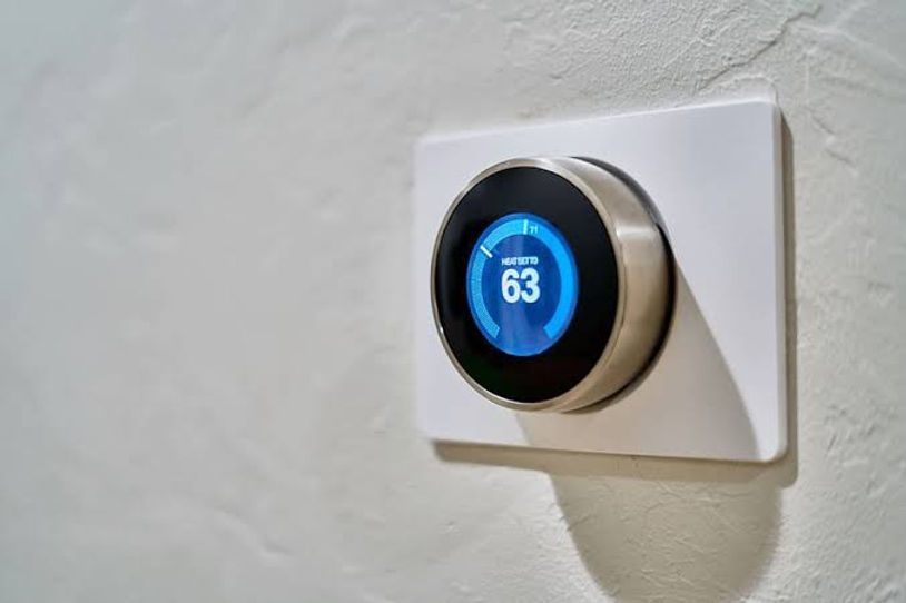 A round smart thermostat with a blue display showing 63 on a white wall.