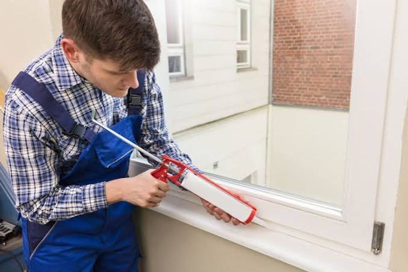 Person using a caulking gun to seal a white window frame indoors