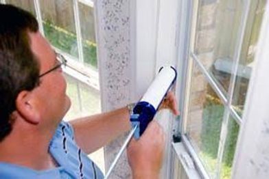 Person caulking a window frame with a blue caulk gun indoors
