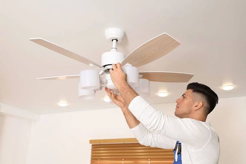 Man replacing a white ceiling fan light bulb with the fan blades extended
