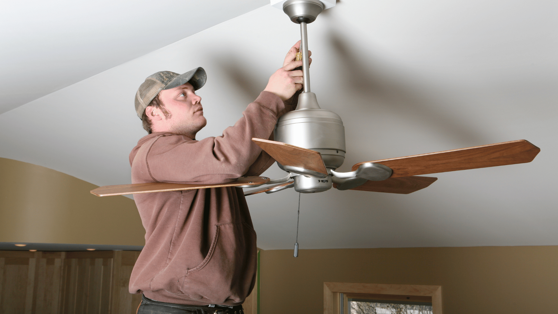 Man installing a ceiling fan with a screwdriver in a living room
