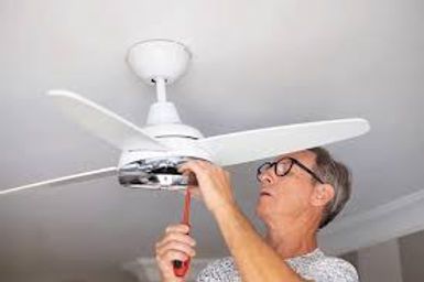 Person tightening screws on a white ceiling fan with a red screwdriver