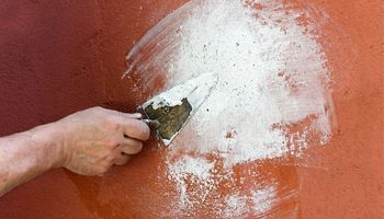 Hand trowel spreading filler on an orange wall