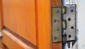 Close-up of a wooden door hinge with metal hardware on a white frame
