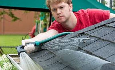 Worker cleaning roof gutters with a hose, wearing a red shirt and white gloves.