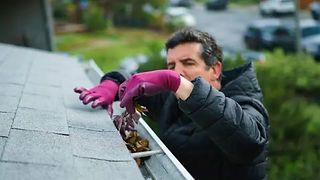 Man in pink gloves cleaning debris from a rooftop gutter with a brush