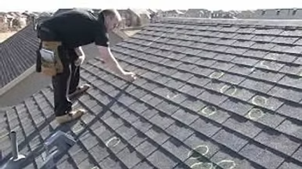 Person inspecting roof shingles with a tool on a sloped house roof.