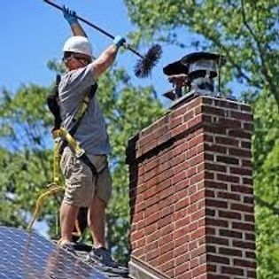 Worker on a roof using a long pole to clean a brick chimney against a blue sky