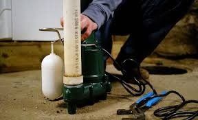 Person operating a green water pump with a white float in a wet basement area