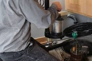 Person in gray sweatshirt pouring liquid from a pot into a kitchen stove-top cooker