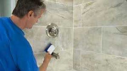 Man cleaning a tiled shower wall with a sponge and spray bottle