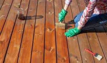 Two people scrubbing a wooden deck with green gloves and brushes