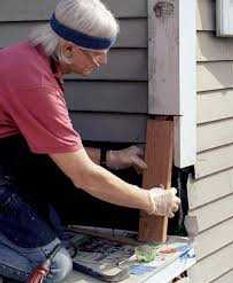 Person painting the exterior of a house window frame with a brush