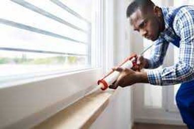 Man caulking a window sill with a caulk gun beside a white window frame