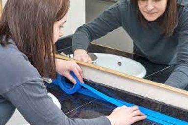 Woman measuring a blue fabric strip on a table in front of a mirror