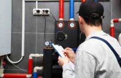 Technician checking boiler gauges with a tablet in a utility room with pipes and valves