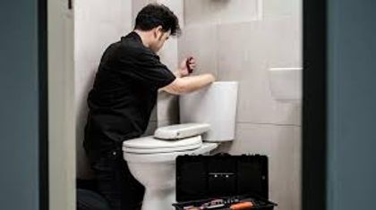 Person in black clothing leaning over a toilet in a bathroom, reaching toward the tank.