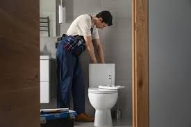 Plumber working in a bathroom beside a toilet, installing a sink with tools on his belt.