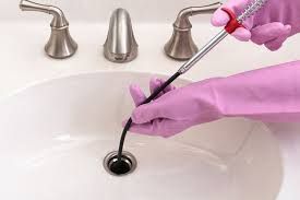 Gloved hands using a pink plunger to unclog a white bathroom sink drain