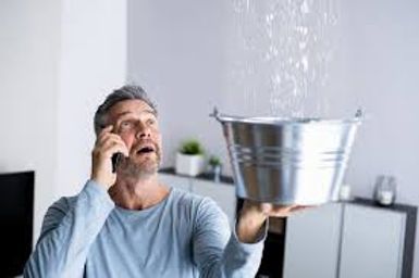 Man on phone holding a metal bucket under a leaking ceiling