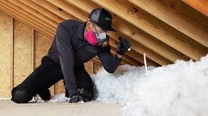Snowboarder in black gear and pink scarf adjusts bindings on a snowy slope under wooden beams