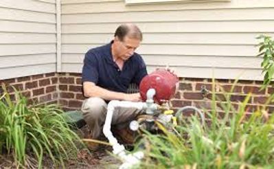 Man kneels by a small dog outdoors beside a house, with a red kettle grill nearby.