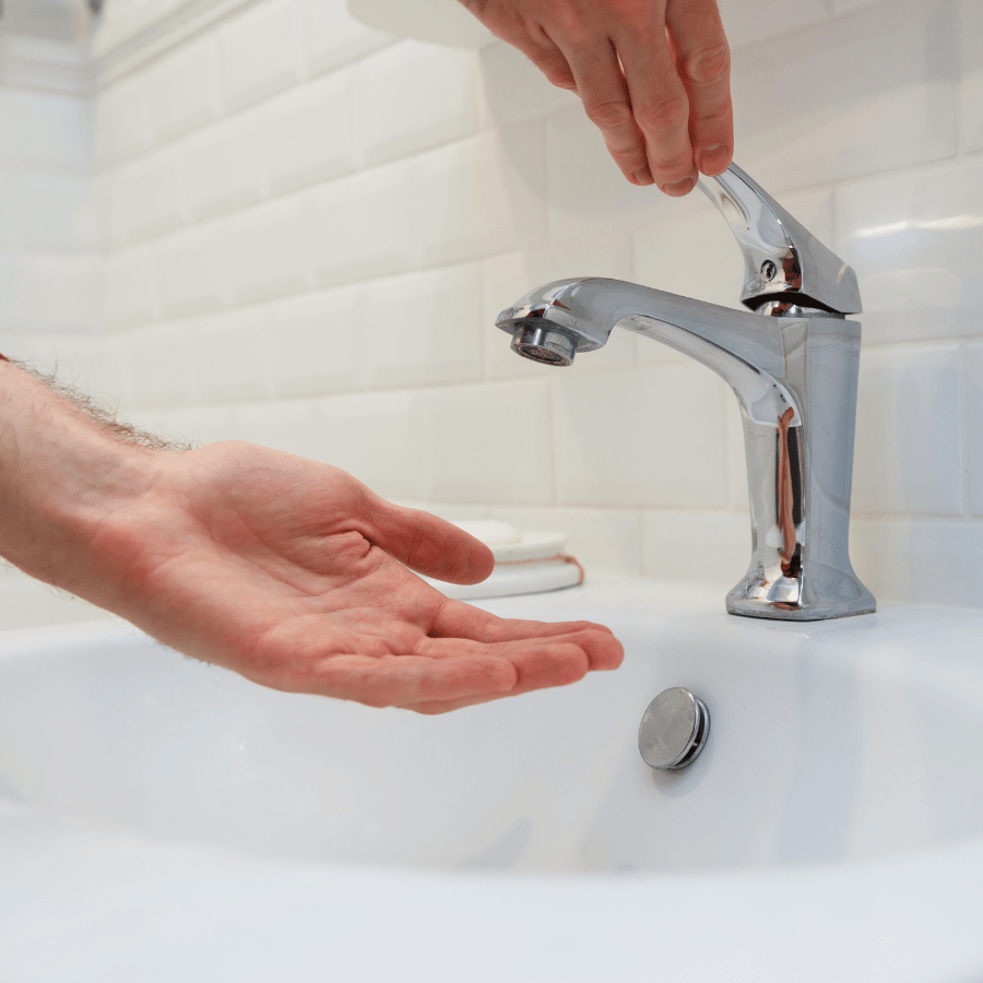 Hands reaching to turn on a chrome bathroom faucet over a white sink