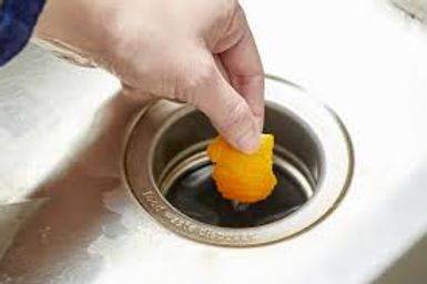 Hand placing a small orange drain deodorizer into a sink drain