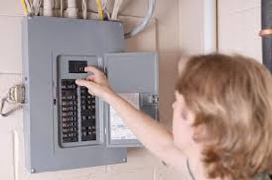 Person reaching into an open gray electrical panel indoors