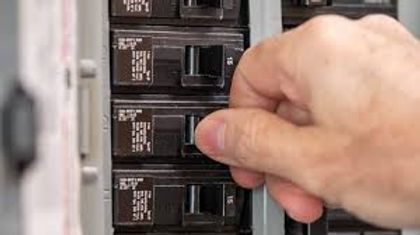 Hand turning a breaker switch on an electrical circuit panel