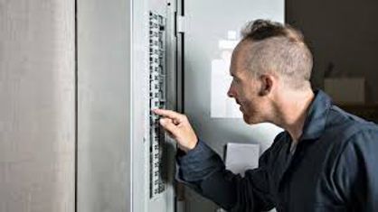 Man adjusting an electrical control panel in a gray utility room