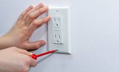 Hand adjusting breakers in an electrical panel with open gray door on a blue wall
