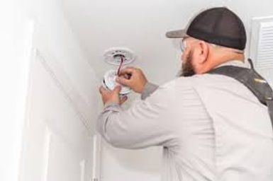 Technician installing a ceiling smoke detector in a white room