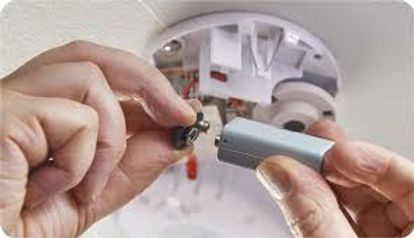 Hands installing a battery in a white smoke detector on the ceiling.
