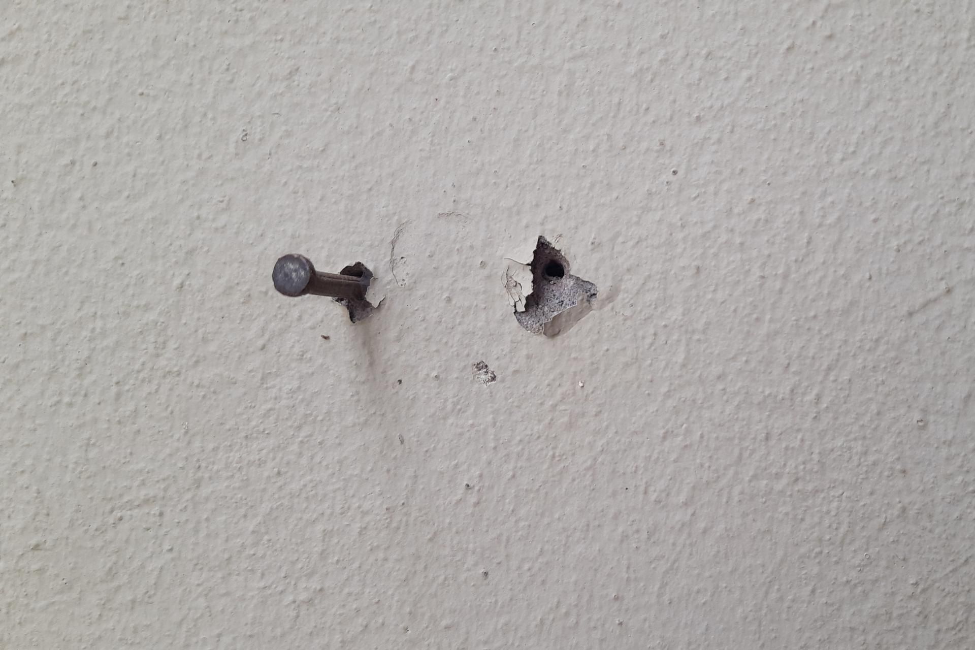 Two wall anchors and a screw in a white textured wall, with one anchor hole damaged